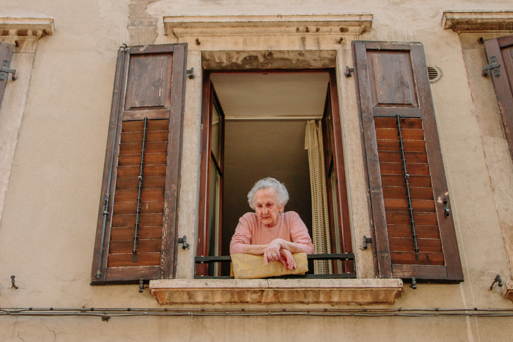 Old Lady Leaning from her balcony chatting to strangers in Trento, Italy